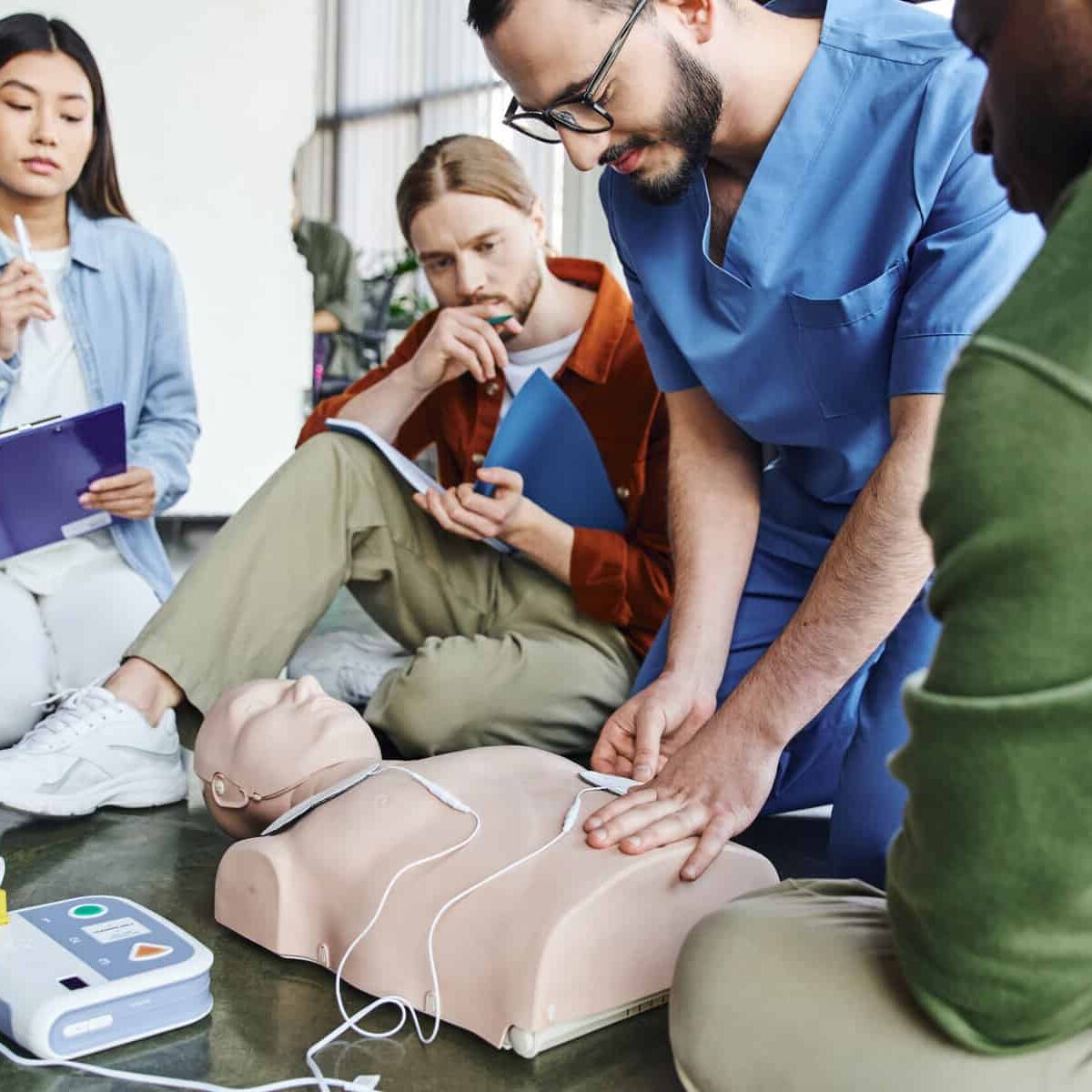 first aid seminar, medical instructor applying defibrillator pads on CPR manikin near multiethnic