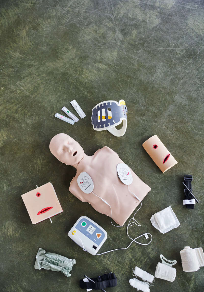 top view of CPR manikin, automated defibrillator, wound care simulators, compression tourniquets, neck brace and bandages, medical equipment for first aid training and skills development